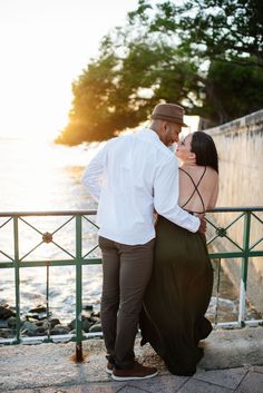 a man and woman standing next to each other near the water with their arms around each other