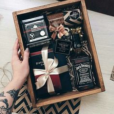 a person's hand is holding a wooden box filled with liquor and gift items