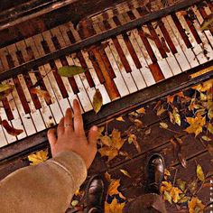 a person standing in front of an old piano with autumn leaves on the ground next to it