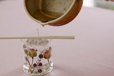 a person pouring water into a glass vase with flowers in it on a pink table cloth