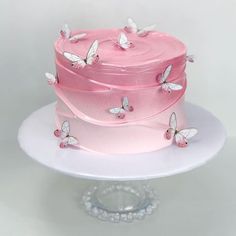 a three layer cake with pink frosting and white butterflies on the top, sitting on a plate