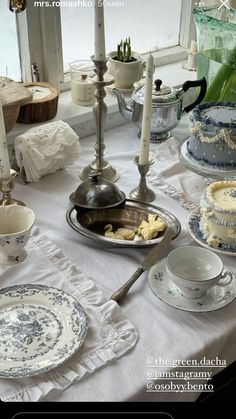 a table topped with plates covered in cake next to candles and other dishes on top of a white table cloth