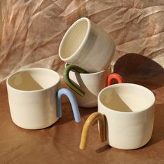 three mugs with handles are stacked on top of each other in different colors and shapes