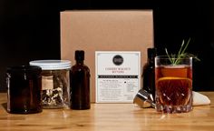 a wooden table topped with bottles and glasses filled with liquid next to a box full of spices