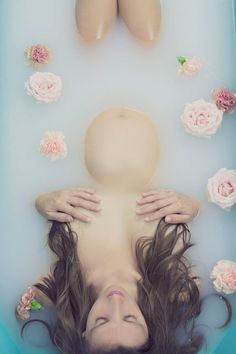 a woman laying in a bathtub with flowers around her head and feet above the water