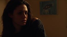 a woman with long brown hair is staring into the distance in a dimly lit room