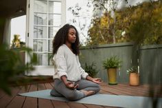 a woman sitting on a yoga mat with her hands in the air while meditating