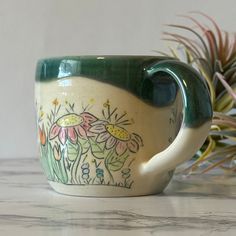 a green and white coffee cup sitting on top of a counter next to a potted plant