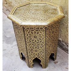 an intricately designed side table sits against a stone wall