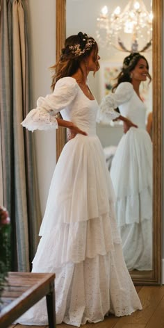 a woman standing in front of a mirror wearing a white dress with ruffles