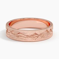 a rose gold wedding band with mountains in the center and an engraved design on it