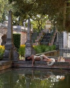 a woman laying on the edge of a pool in front of some stairs and trees