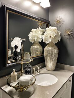 a bathroom sink with two vases on top of it and flowers in the mirror