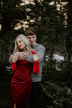 a man and woman standing next to each other in front of some trees with their arms around each other