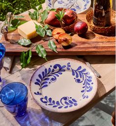 the table is set with blue and white dishes, wine glasses, cheese board, and fruit