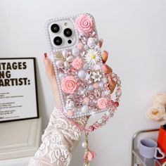 a woman is holding up her phone case with flowers on the back and pearls attached to it