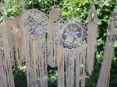 several white macrame dream catchers hanging in the grass next to some trees