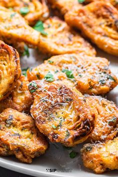 some fried food on a white plate with parmesan cheese and green herbs in the middle