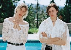 two women standing in front of a pool with their arms crossed and looking at the camera