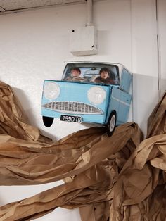 a blue car with two people in the front driving through some brown paper streamers