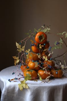 an arrangement of oranges and blue berries on a white table cloth with leaves around them