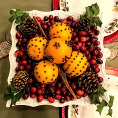 oranges, cranberries and pine cones are arranged in a bowl on a table