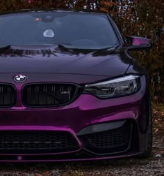 the front end of a purple car parked on top of a gravel road next to trees