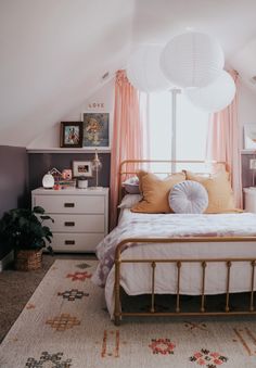 a white bed sitting under a window next to a dresser and lamp on top of a rug