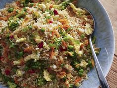 a blue bowl filled with rice and veggies next to a fork on top of a wooden table