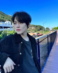 a young man is standing on a bridge with his hand in his pocket and looking at the camera