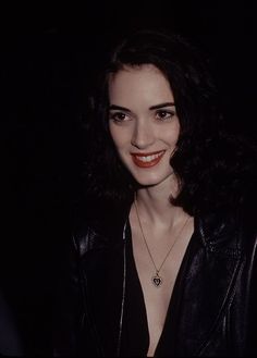 a woman wearing a black leather jacket and smiling at the camera with red lipstick on her lips