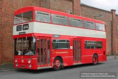 a red and white double decker bus parked in front of a brick building on the street