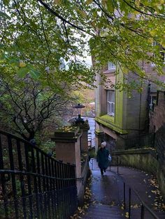 a woman walking down a set of stairs next to a tall brick building on a rainy day