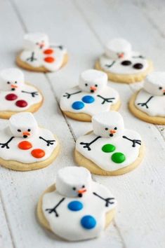 decorated cookies are arranged in the shape of snowmen on a white wooden surface with colored icing