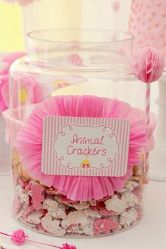 a glass jar filled with pink and white candies next to a sign that says animal crackers