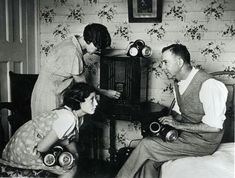 three people sitting on a bed with dumbs in front of an old fashioned radio