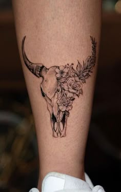 a tattoo on the leg of a woman with flowers and a bull's skull