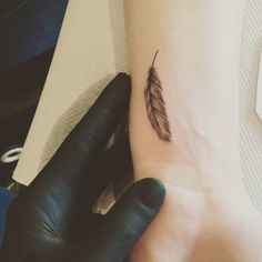 a small feather tattoo on the left inner forearm and wristband is shown in black ink