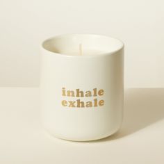 a white candle with the words inhale exhale written on it next to a cup