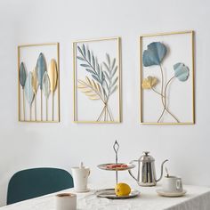 three framed art pieces on the wall above a table with teapots and fruit