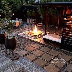 an outdoor fire pit surrounded by wooden decking and graveled area with potted plants