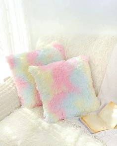 three fluffy pillows sitting on top of a white couch next to a book and pillow