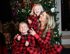 a woman and two children in matching pajamas sitting on the floor next to a christmas tree