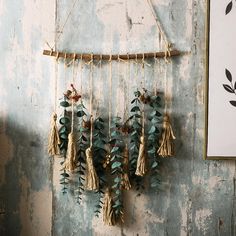 a wooden wall hanging with tassels and leaves on it next to a painting