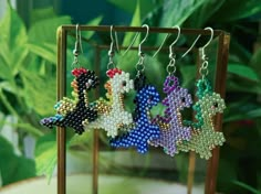 four pairs of beaded earrings are hanging from a wooden stand in front of some plants