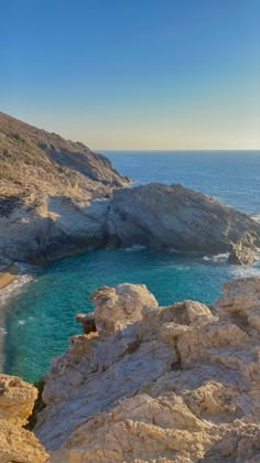 a rocky cliff overlooks the ocean with clear blue water and rocks on either side