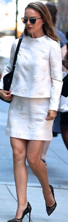 the woman is walking down the street in her white dress and black heels, carrying a purse