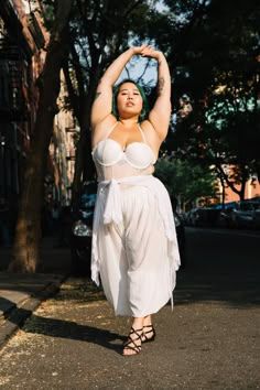 a woman in a white dress is standing on the street with her hands up to her head