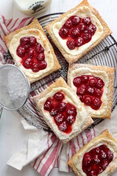 four pastries on a cooling rack with powdered sugar and cherries in the middle