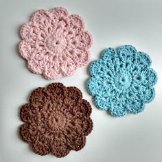 three crocheted flowers sitting on top of a white table next to each other